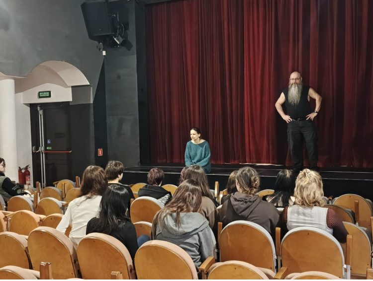 scena na niej stoi aktor z długą brodą, uczniowie siedzą na widowni, słuchają wykładu