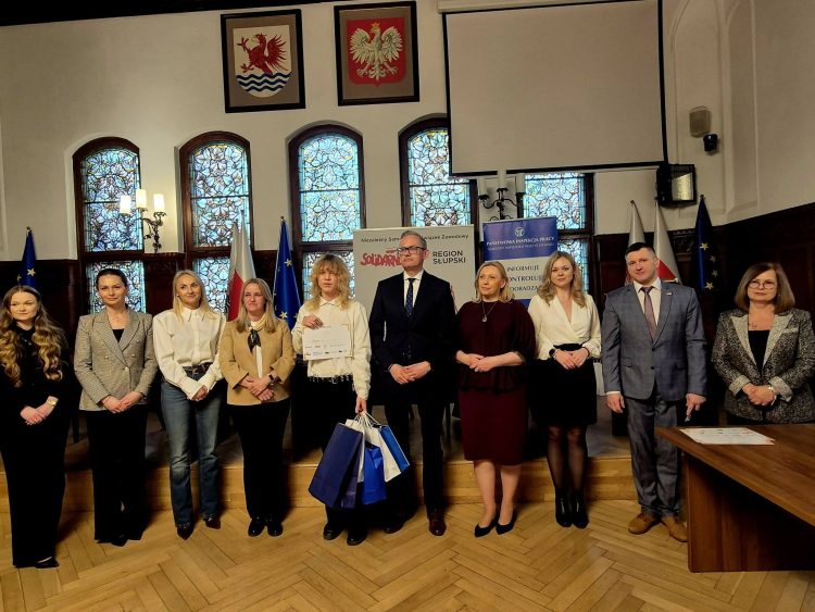 ludzie stojący w szeregu, w środku uczeń odbierający nagrodę